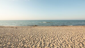 Ein Sandstrand mit sanften Wellen und blauem Himmel.