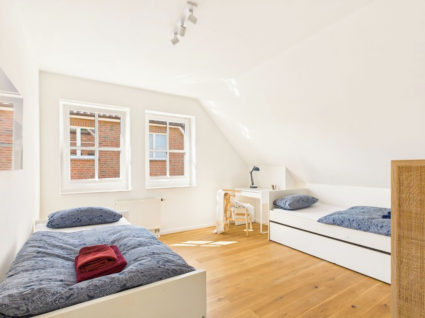 A bedroom with a sloped ceiling, two beds, a desk, and a chair.