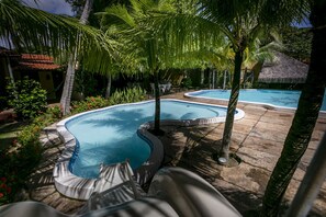 A pool area with two pools, surrounded by palm trees and a stone patio. - Pousada do Sol (Aquiraz)