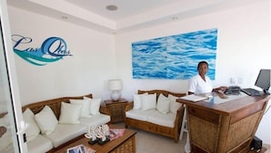 Un espace d’accueil avec une réceptionniste, deux canapés blancs, un bureau en bois et un grand tableau représentant un paysage marin accroché au mur.