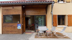 A wooden building with a sliding glass door entrance, a small patio with metal chairs, and a sign indicating a restaurant or dining area. - Le Grand Noyer (Ambronay)