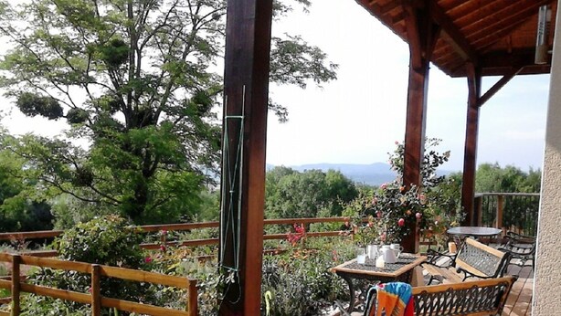 A covered outdoor area with wooden furniture, a table with a cup, and a bench. - Le Grand Noyer (Ambronay)