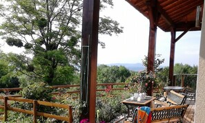 A covered outdoor area with wooden furniture, a table with a cup, and a bench. - Le Grand Noyer (Ambronay)