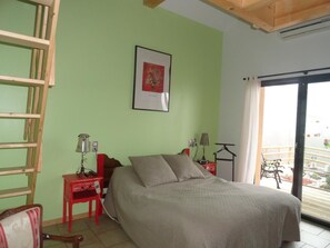 A bedroom with a bed, two bedside tables with lamps, a wooden ladder, a framed picture on the wall, and a balcony with a railing. - Le Grand Noyer (Ambronay)