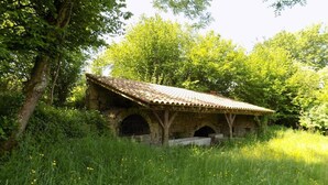 A rustic stone building with a tiled roof, surrounded by lush greenery and trees. - Le Grand Noyer (Ambronay)