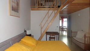 A bedroom with a bed, a wooden staircase, a dining area, and a view of the outdoors. - Le Grand Noyer (Ambronay)