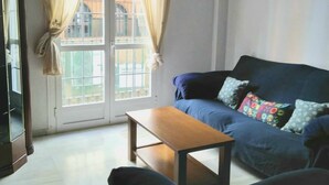 Een woonkamer met een blauwe bank, een houten salontafel en een groot raam met gordijnen.