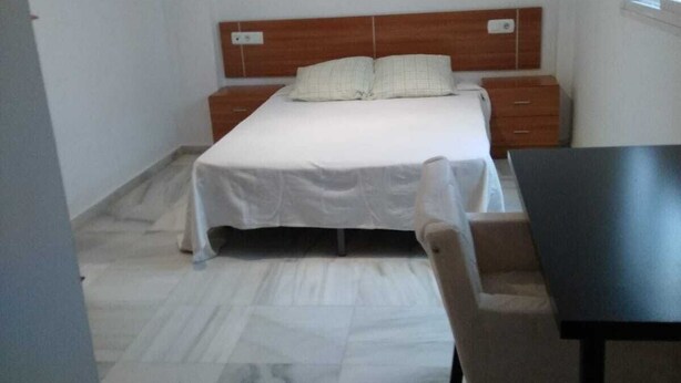 Een slaapkamer met een bed, een houten hoofdbord, een nachtkastje en een stoel.