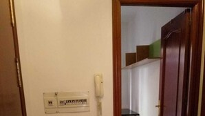 Een gang met een telefoon, stopcontacten en een deur naar een andere kamer.
