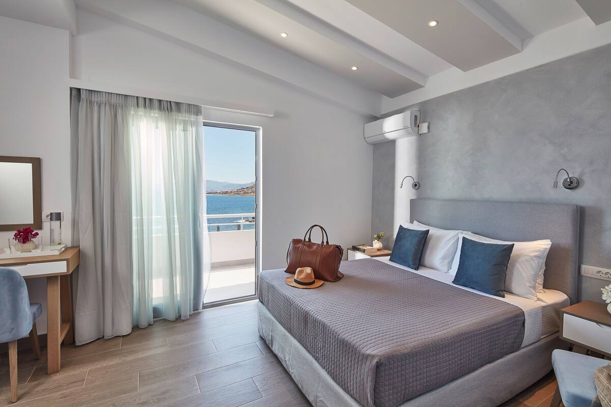 A modern bedroom with a large bed, a desk, and a view of the sea.