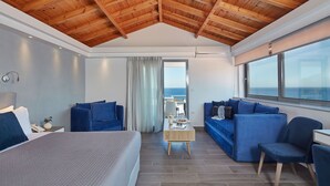 A modern hotel room with a wooden ceiling, a large bed, blue sofas, and a view of the sea. - Alkinoi Resort & Spa (Monemvasia)