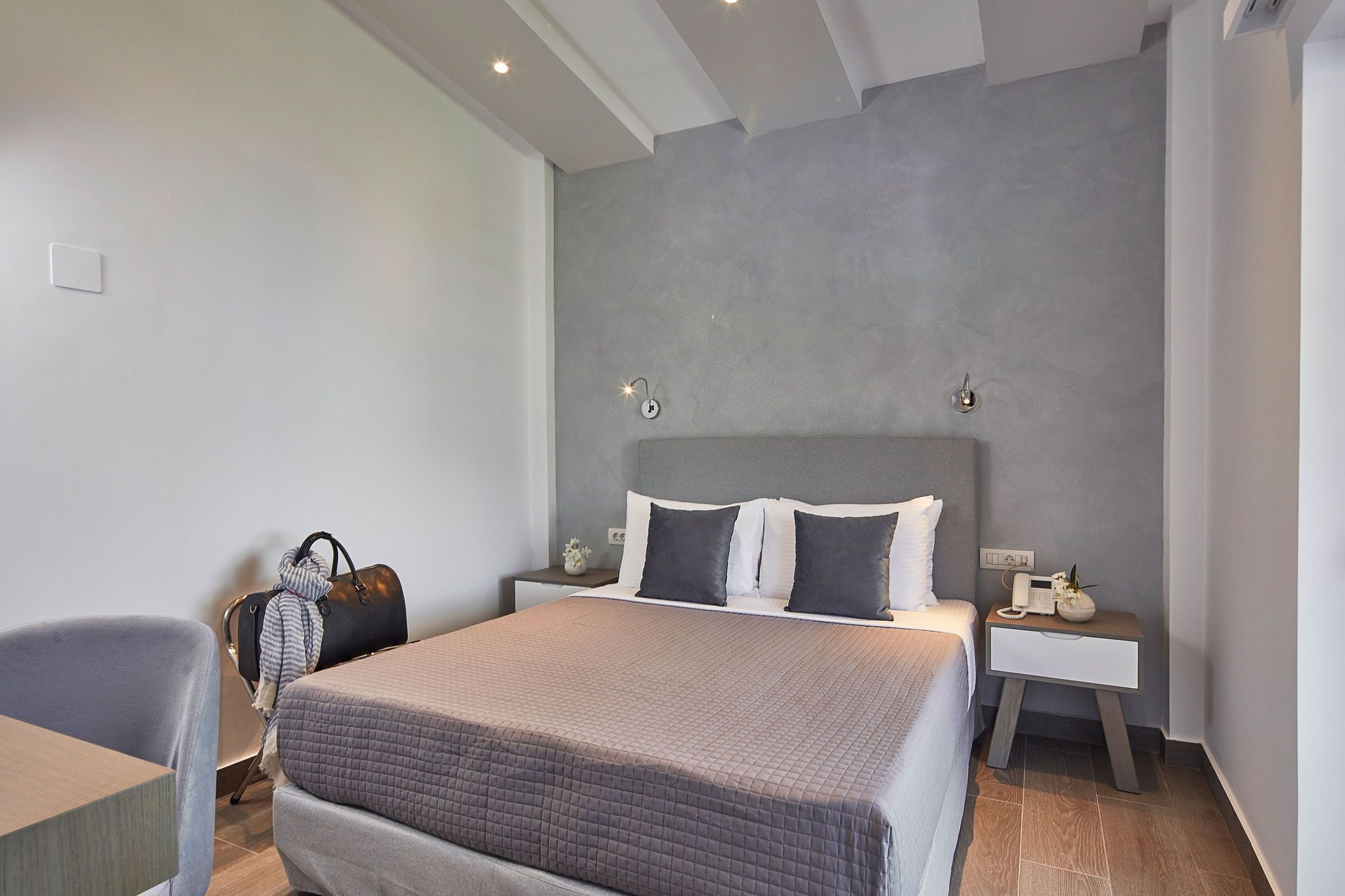 A modern bedroom with a large bed, a nightstand, a chair, and a suitcase.