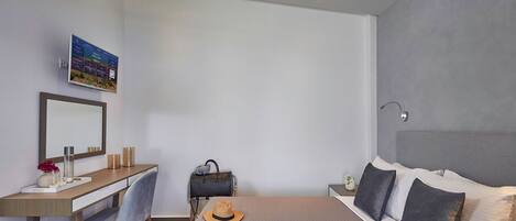 A modern hotel room with a bed, a desk, a chair, a handbag, a hat, and a framed picture on the wall.