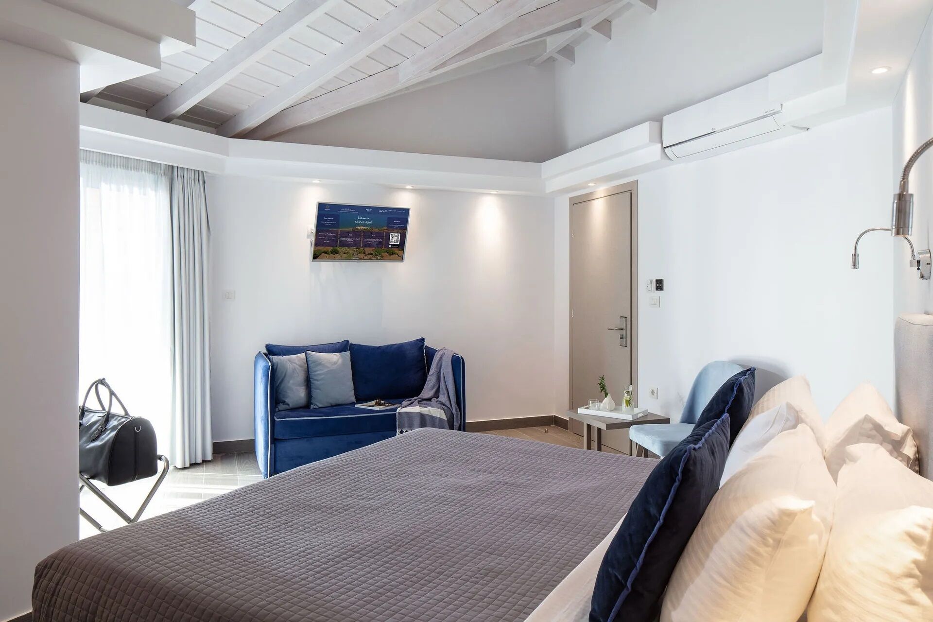 A modern hotel room with a large bed, a blue sofa, a small table, and a chair.