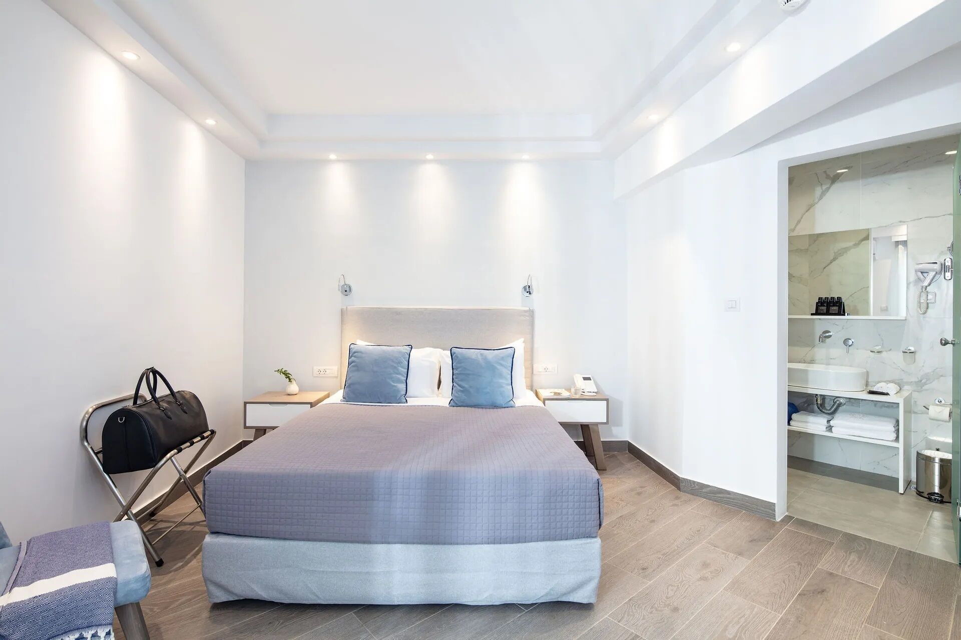 Ein modernes Hotelzimmer mit einem großen Bett, Nachttischen, einem Schreibtisch und einem durch eine offene Tür einsehbaren Badezimmer.