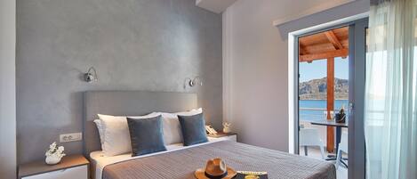 Una habitación de hotel moderna con una cama grande, una mesita de noche con teléfono y jarra, y un balcón con mesa y sillas.