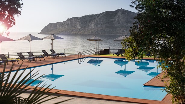 A pool with lounge chairs and umbrellas, a view of the sea, and a mountain in the background. - Alkinoi Resort & Spa (Monemvasia)