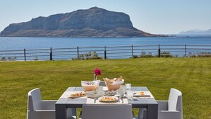 A table set for a meal with a view of a large mountain and a body of water. - Alkinoi Resort & Spa (Monemvasia)