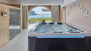 A modern spa area with a hot tub, a view of the sea, and a wooden cabinet with a control panel. - Alkinoi Resort & Spa (Monemvasia)