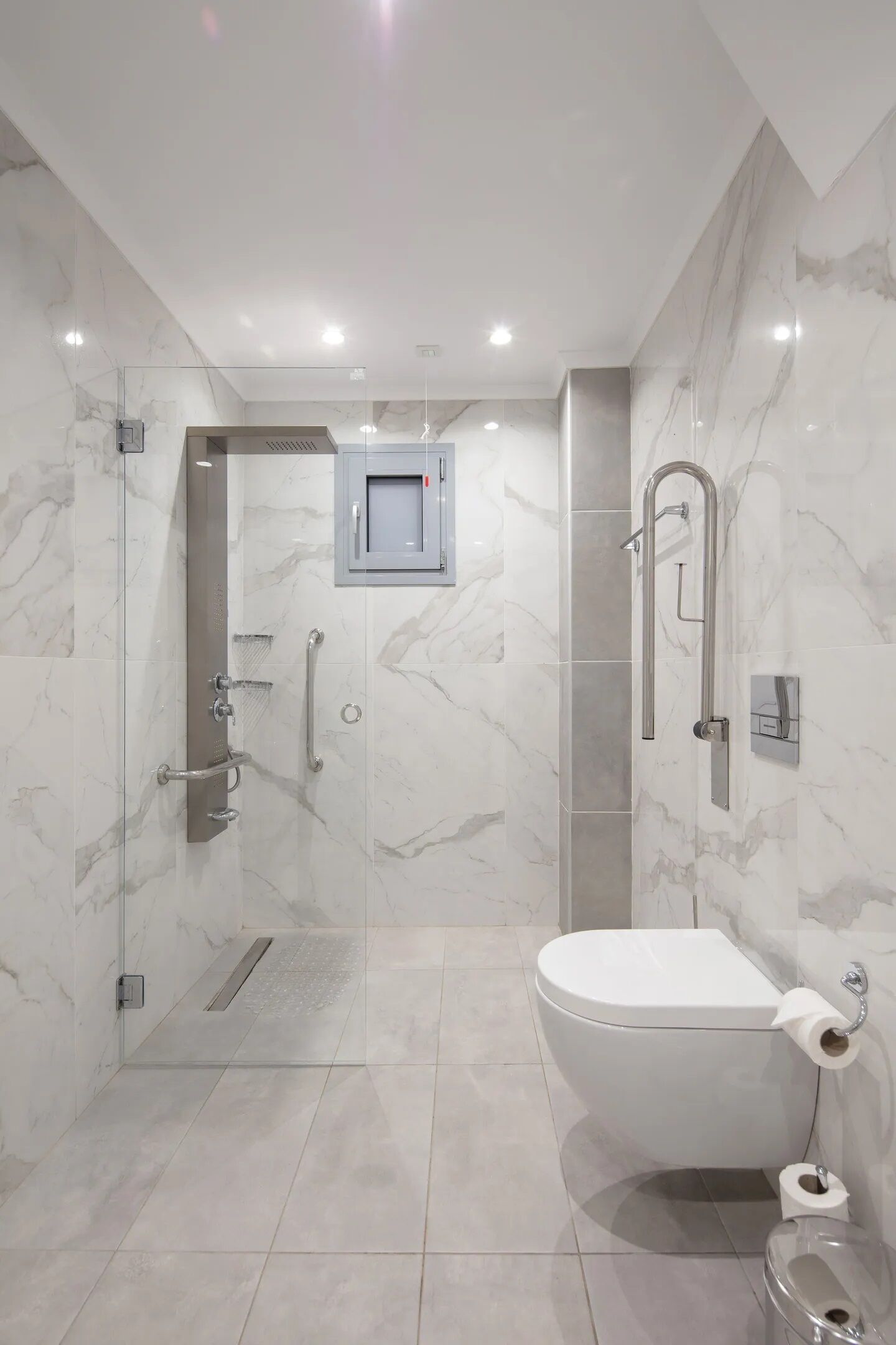 Ein modernes Badezimmer mit einer gläsernen Duschkabine, einer Toilette und einer Marmorwand.