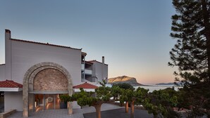 A modern building with a stone archway entrance, a balcony, and a view of the sea at sunset. - Alkinoi Resort & Spa (Monemvasia)