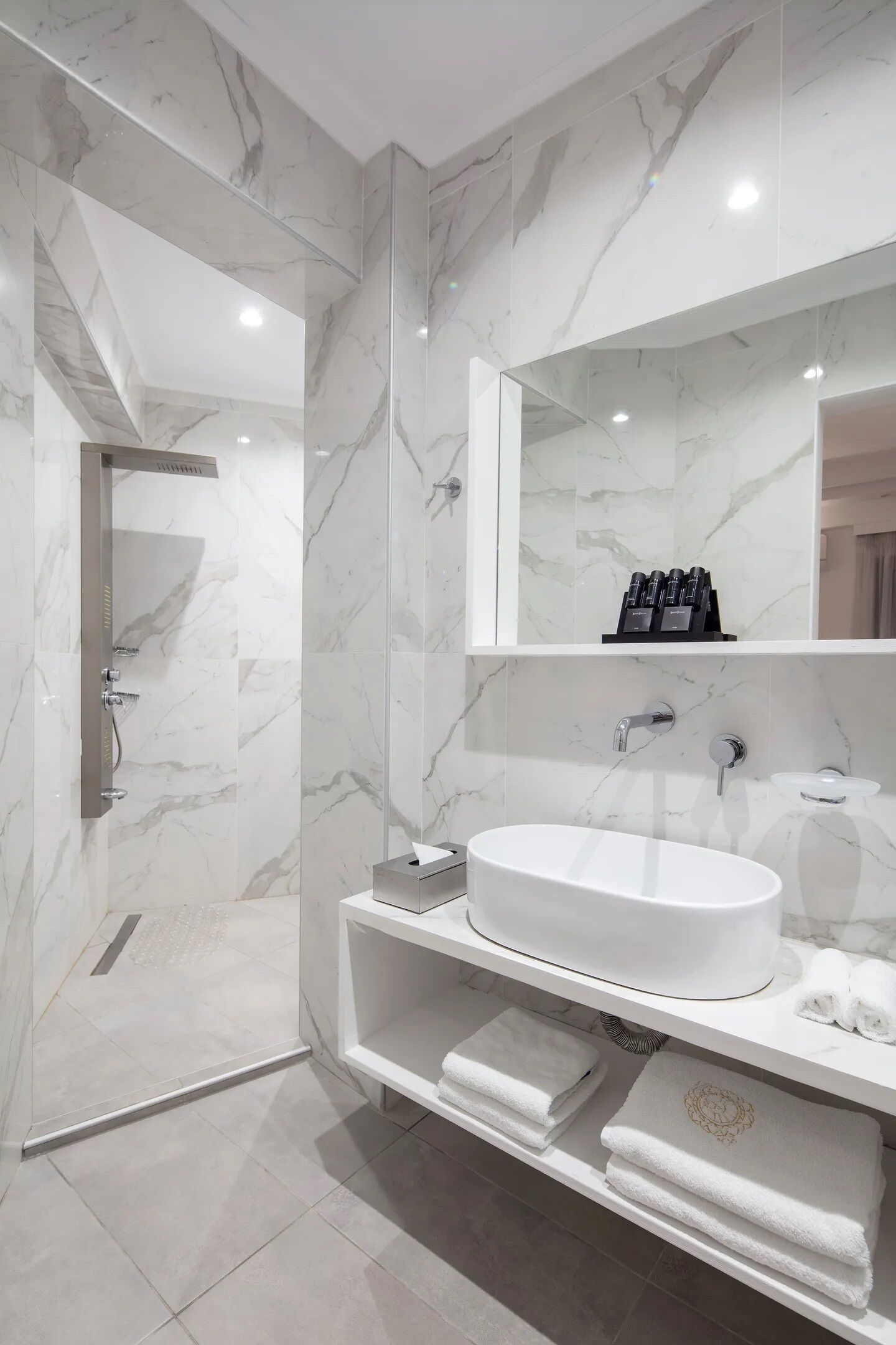 Ein modernes Badezimmer mit einer Marmordusche, einem großen Spiegel und einem weißen Waschbecken.