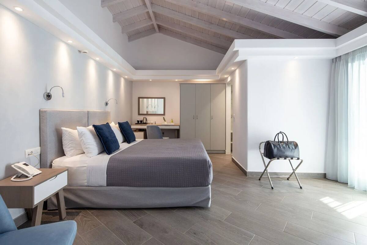 A modern hotel room with a large bed, a desk, a chair, and a wardrobe.