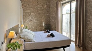 A bedroom with a stone wall, a bed with white linens, a bedside lamp, and a potted plant. - Rural House La Païssa (Ullà)