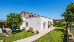Ein modernes, zweistöckiges Haus mit gepflasterter Auffahrt, einem kleinen Garten mit Kübelpflanzen und blauem Himmel.