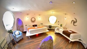 A modern bedroom with a large bed, two smaller beds, a chair, and a unique circular window. - Wifala Harmony Hotel (Urubamba)