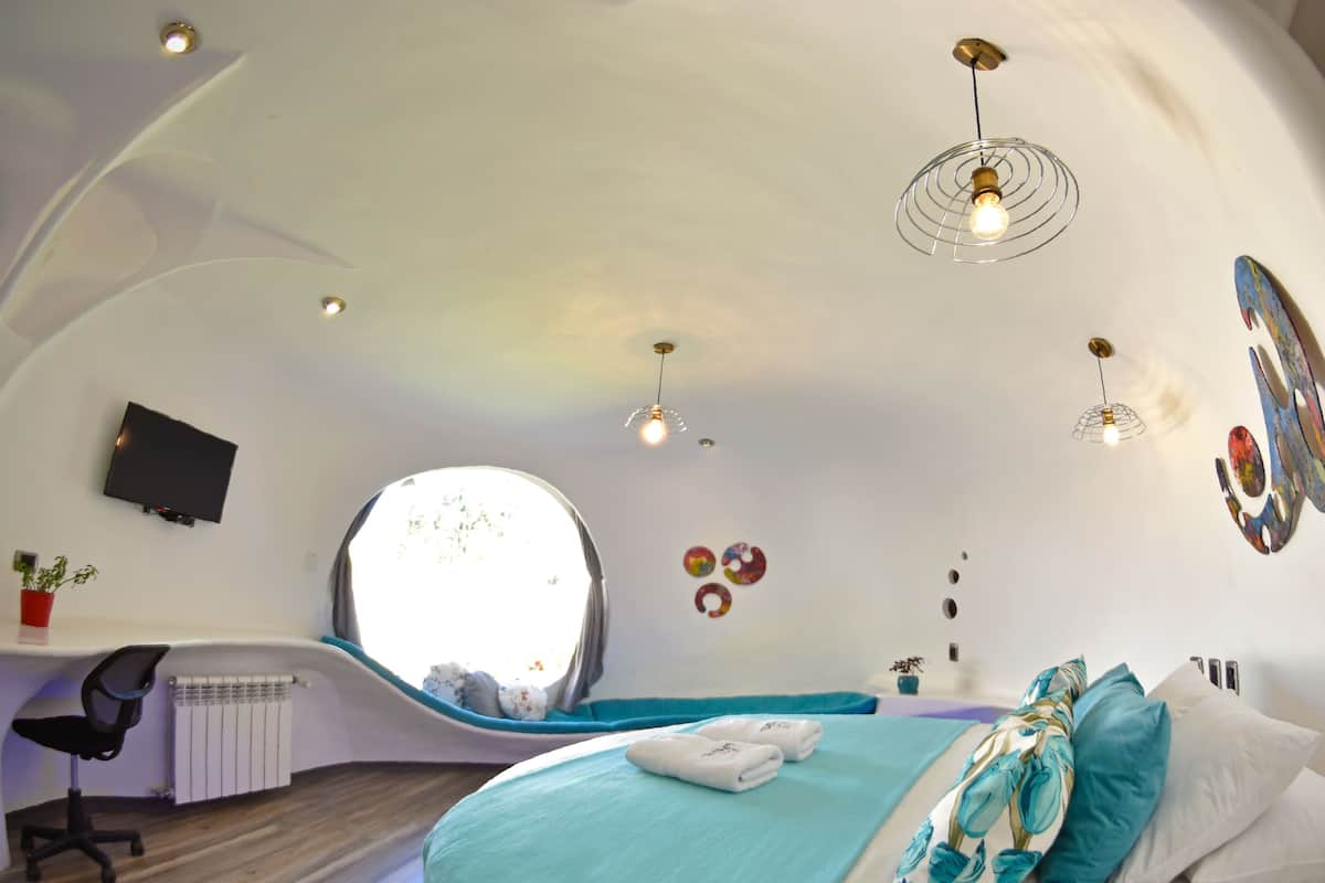 Quarto moderno e curvo, com uma cama, uma escrivaninha e uma televisão.