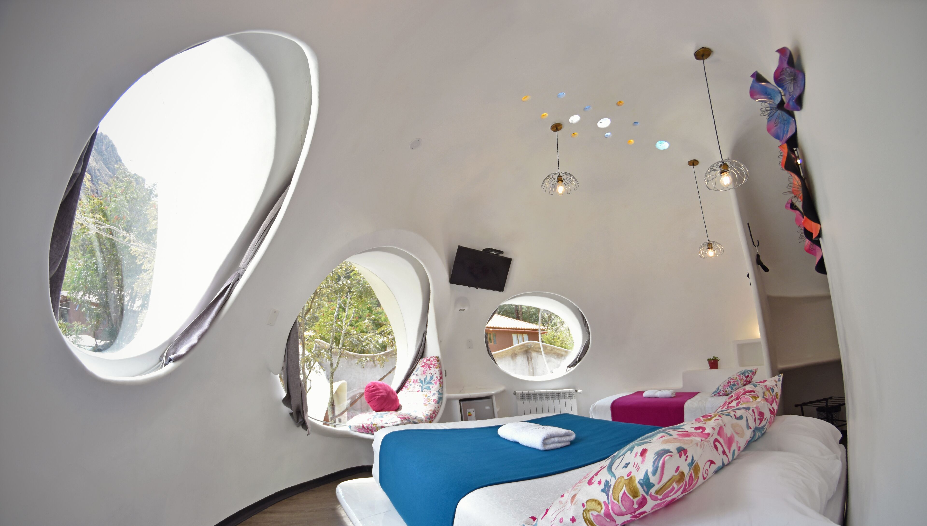 Une chambre moderne avec un grand miroir, deux petits miroirs, un lit recouvert d’une couverture bleue, un téléviseur fixé au mur et un luminaire au plafond.