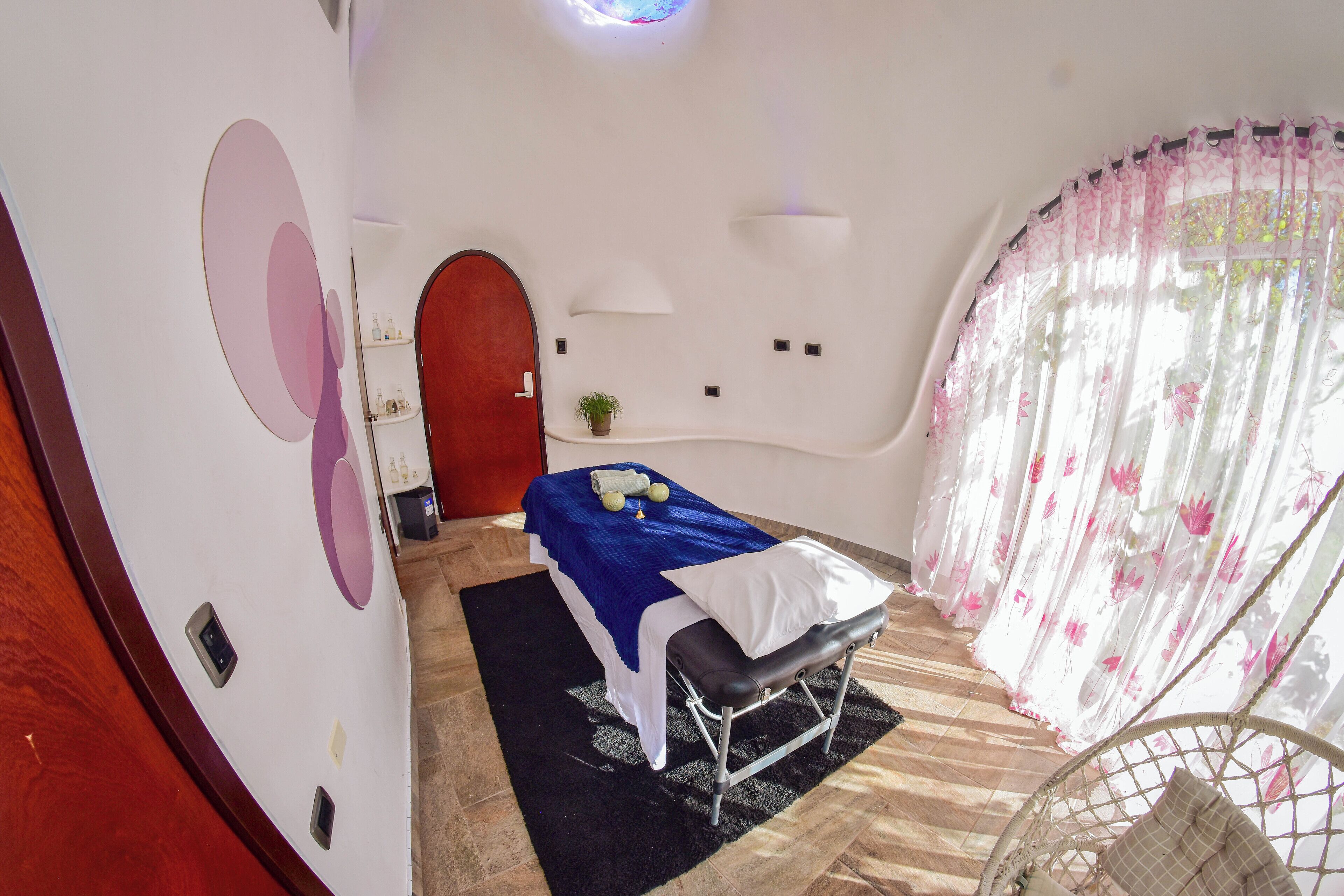 A room with a bed, a chair, a small table with a plant, and a door.