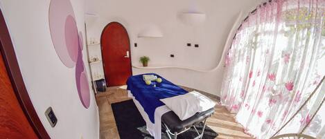 A room with a bed, a chair, a small table with a plant, and a door.