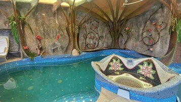 Una piscina interior con mosaicos, un banco decorativo y obras de arte en la pared.