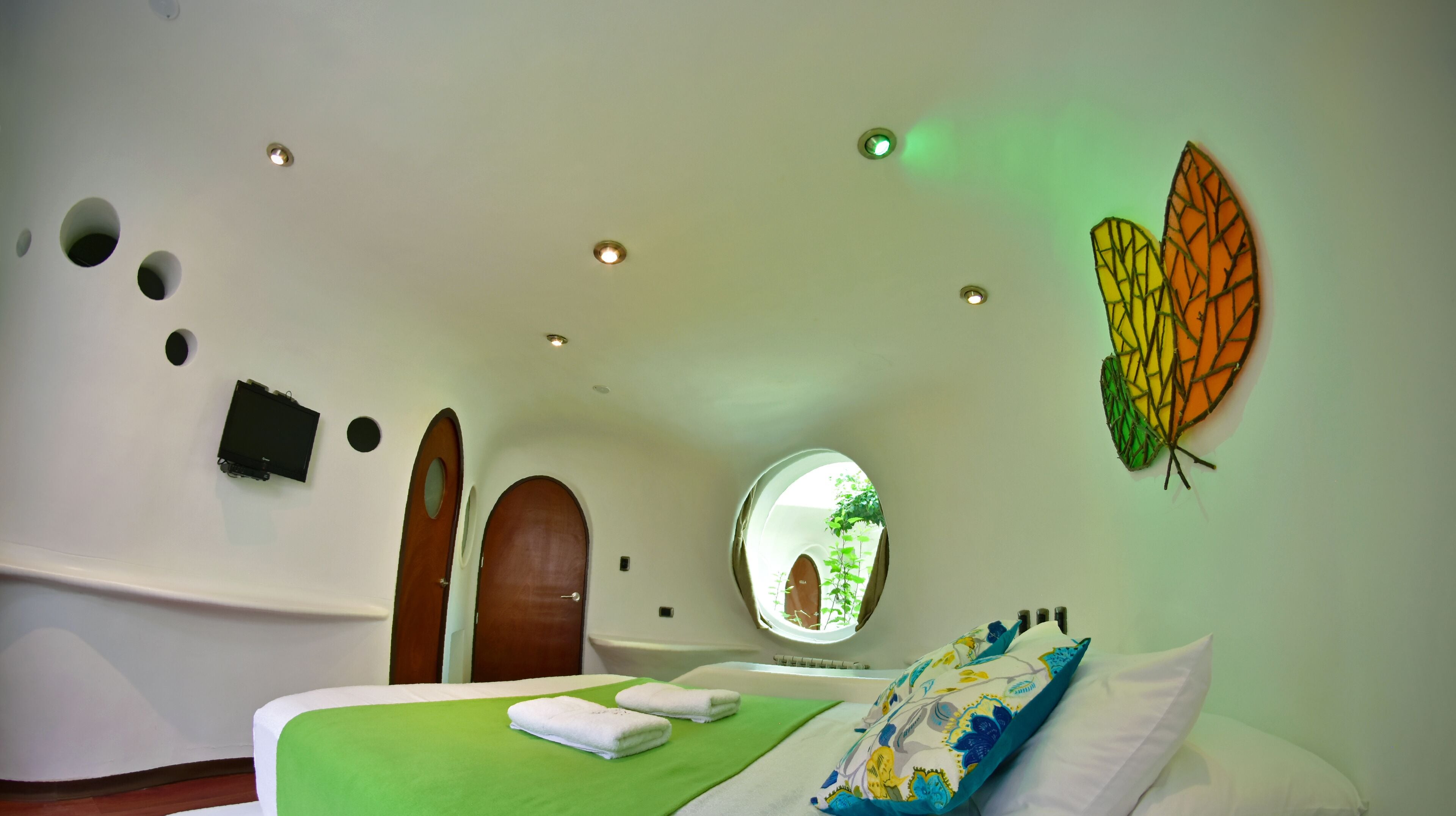 A bedroom with a green bedspread, two towels, a butterfly wall art, and a circular window.