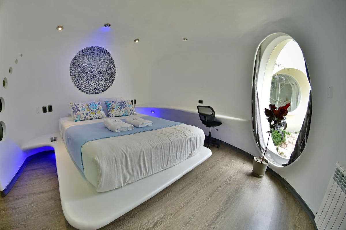 Um quarto moderno com um domo circular no teto, uma decoração redonda na parede e uma cama com iluminação azulada.