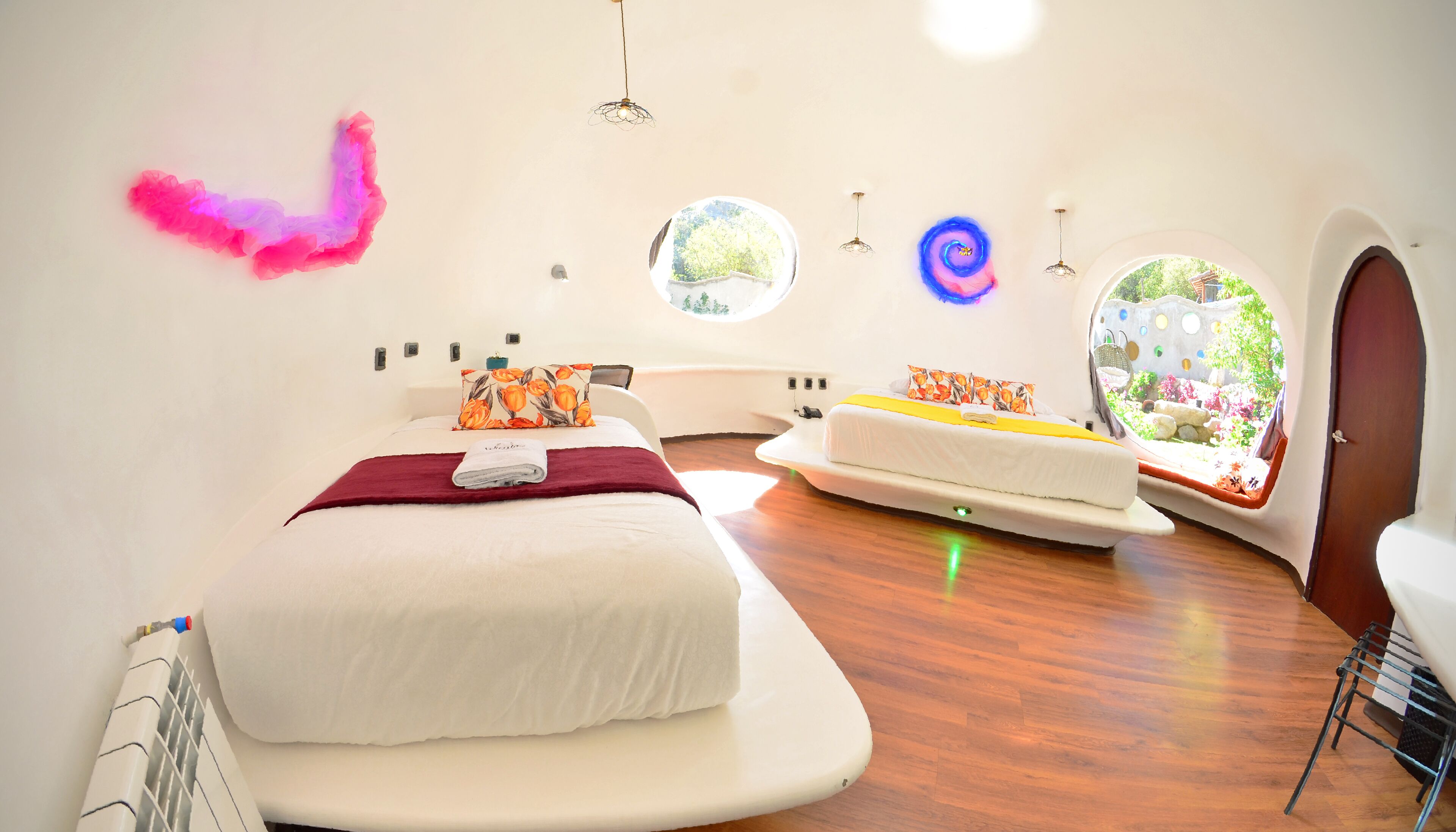 Een moderne slaapkamer met een groot bed, een kleiner bed, en een raam met uitzicht op groen.