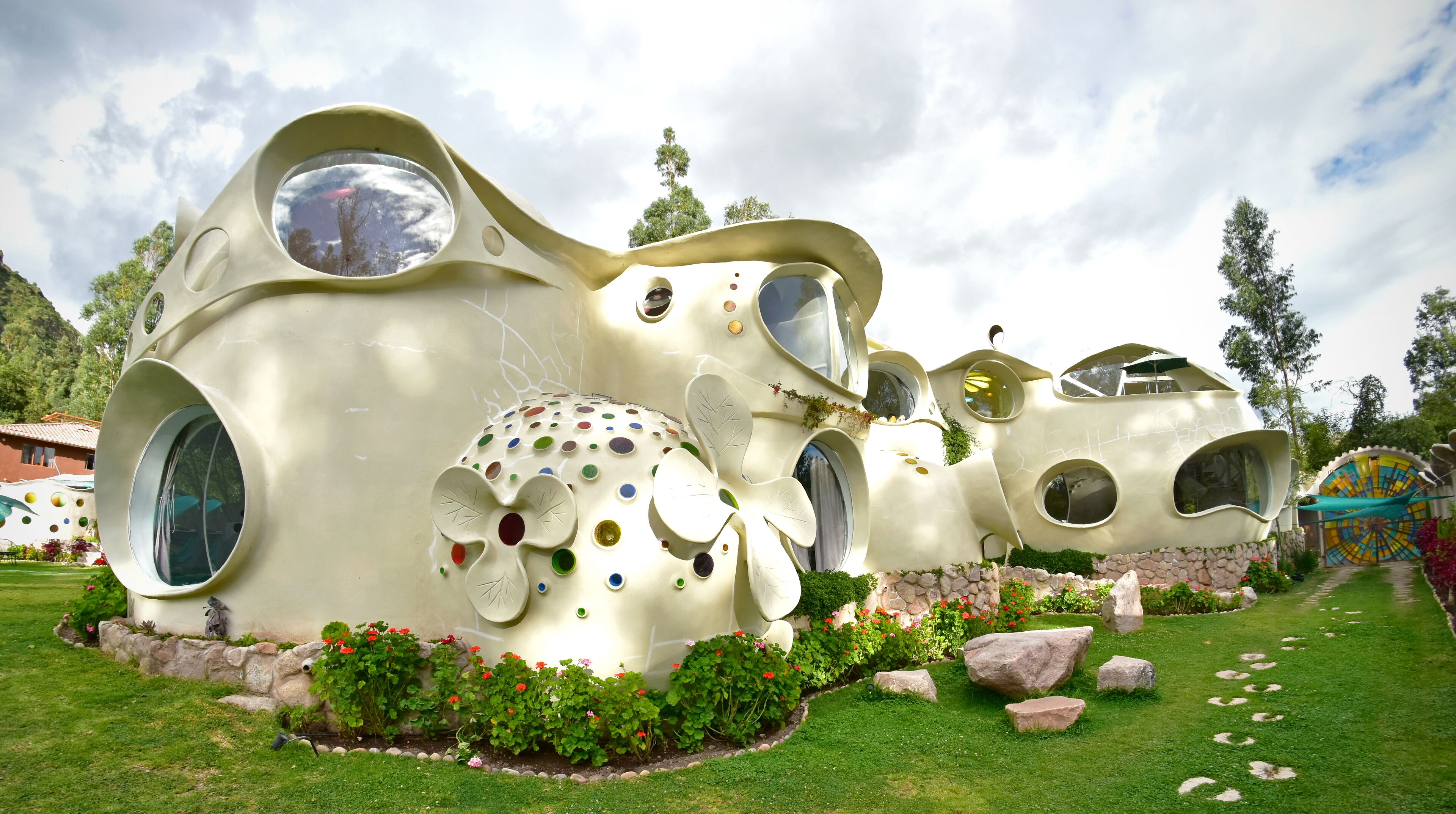 A unique, organic-style building with multiple circular windows and a garden area with rocks and flowers.