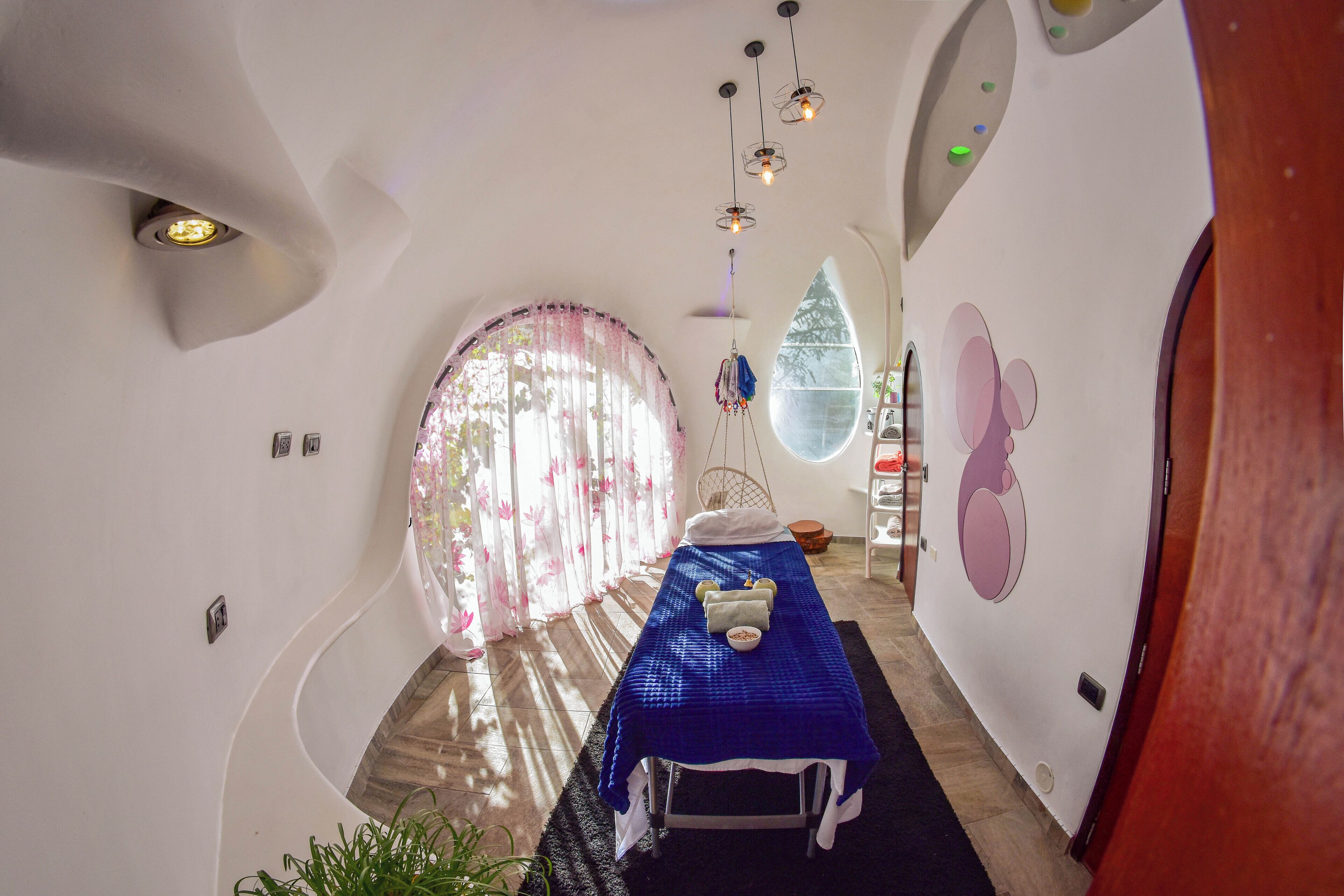 A modern room with a curved ceiling, a massage table, and a large window with curtains.