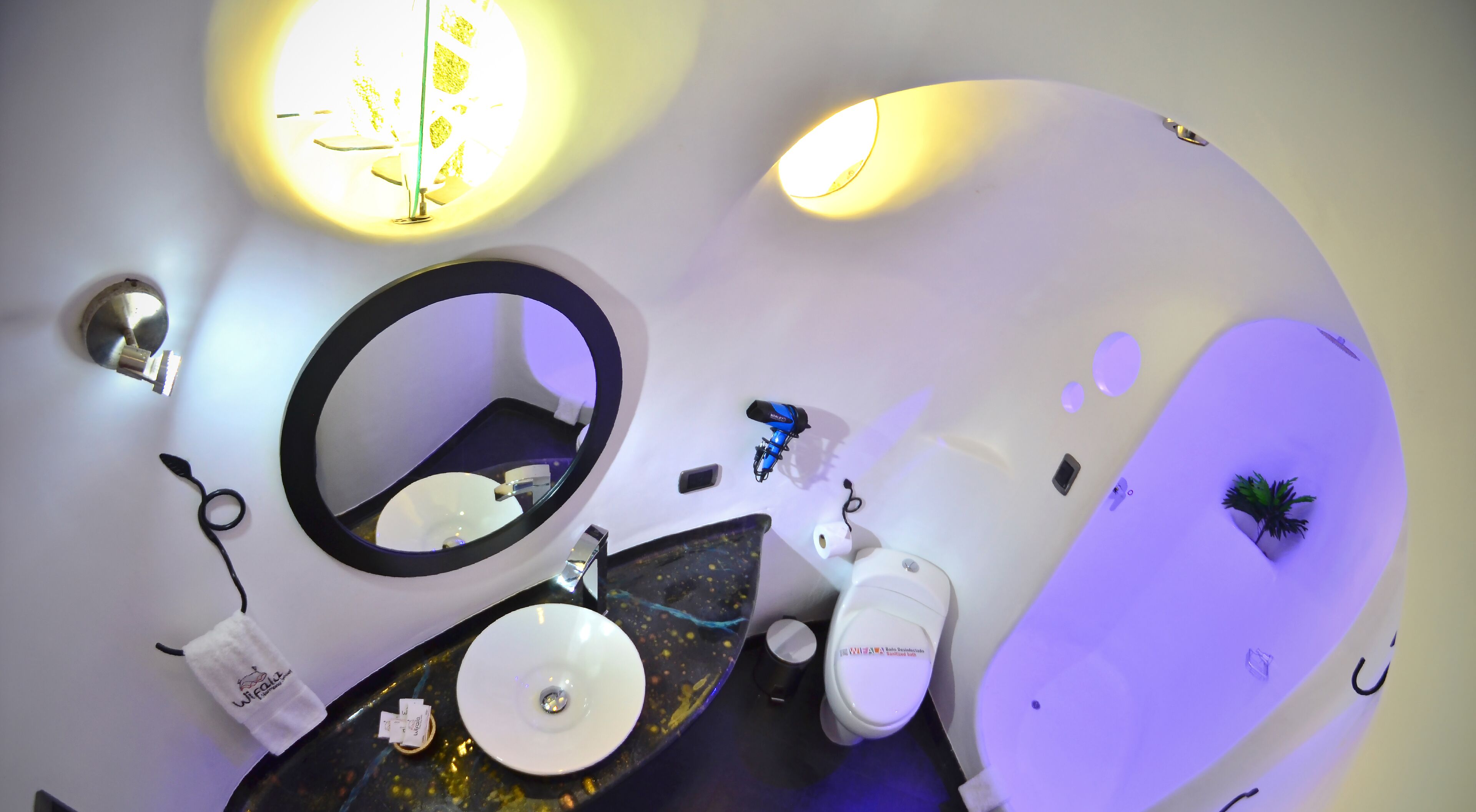 A modern bathroom with a round mirror, two sinks, and a toilet.