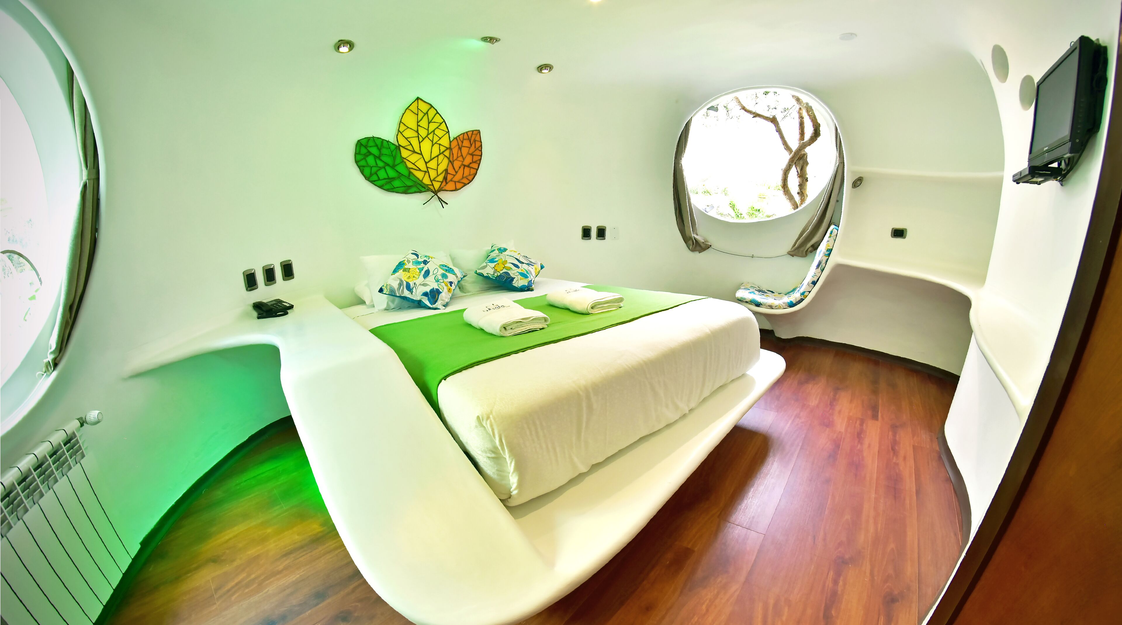 Une chambre à coucher moderne et compacte, avec un lit, une couvre-lit verte et un téléviseur fixé au mur.