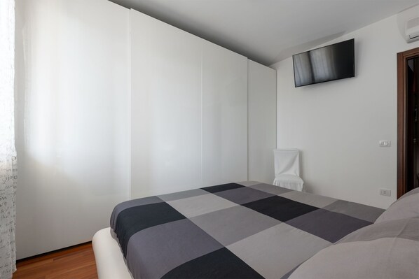 A bedroom with a bed, a flat-screen TV mounted on the wall, and a white curtain on the window. - Casa dei Gufi Superior Apartment (Foligno)