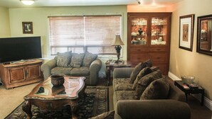 A living room with a sofa, armchair, coffee table, TV, and a cabinet with glassware.