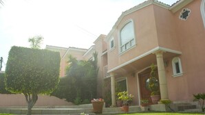 A two-story house with a pink facade, a front porch with columns, and potted plants.