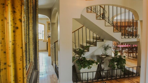 A staircase with ornate metal railings, leading to a dining area with wooden furniture and potted plants.