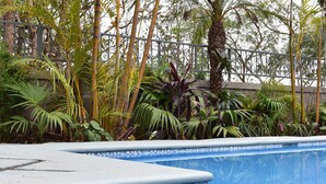 A swimming pool with a tiled edge, surrounded by various tropical plants and a metal fence. - Liquidambar Hotel (Santa Lucia)