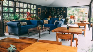 A cozy living room with a blue sofa, wooden tables, and chairs, surrounded by potted plants and large windows. - Liquidambar Hotel (Santa Lucia)