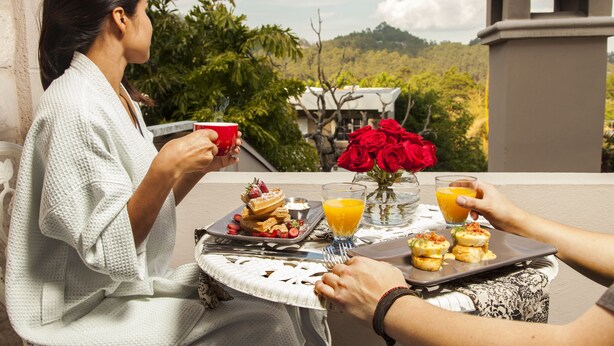 A dining table with breakfast items, a vase of red roses, and a scenic view. - Liquidambar Hotel (Santa Lucia)