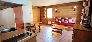 Une petite cuisine équipée d’un évier, d’une cuisinière et d’une table en bois, ainsi qu’un banc en bois avec des coussins rouges et une fenêtre avec des rideaux.